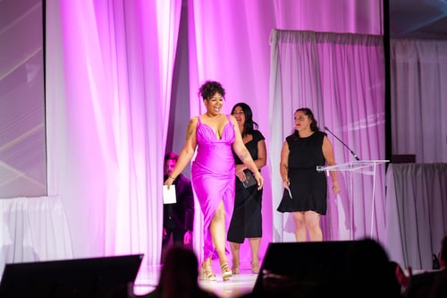 Woman walking on pink lit stage during awards event