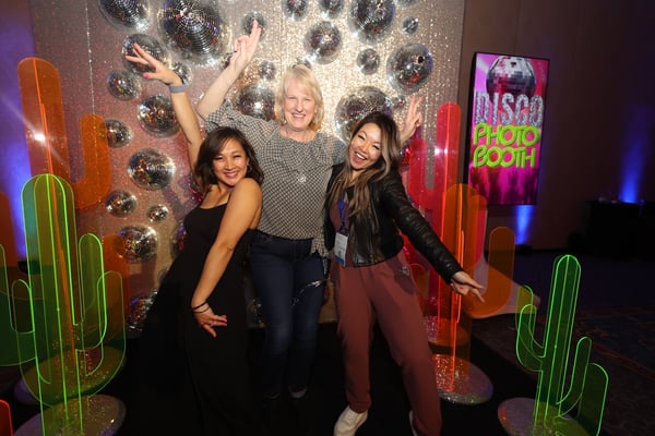 Two women pose in front of creative photo wall at corporate event