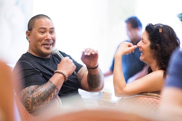 Smiling man talking into with microphone while female coworker looks on and laughs.