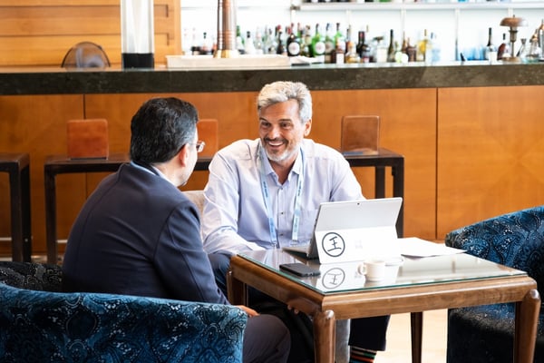 Two men talk at a table with a laptop open 