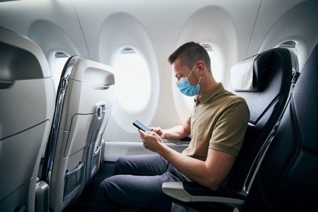 masked man looks at tablet while on flight 1265181396