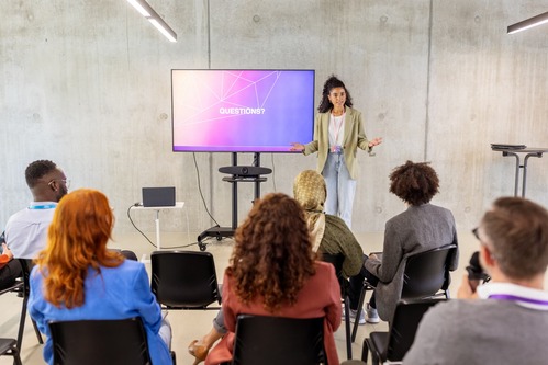 Woman standing next to a monitor speaking to a small audience