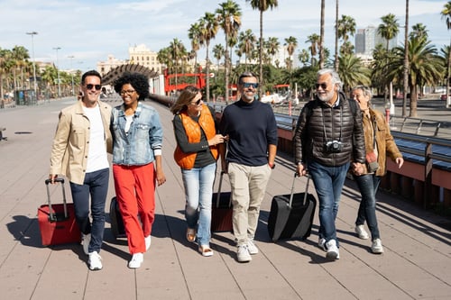 Group of people walking together with suitcases on a boardwalk with palm trees