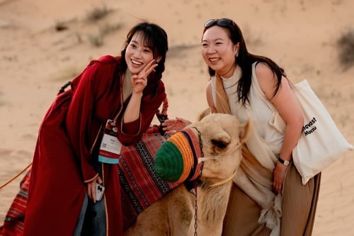Young women posing with a camel in the sand