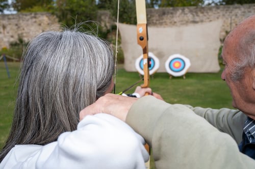 Man helping a woman aim an arrow at a target