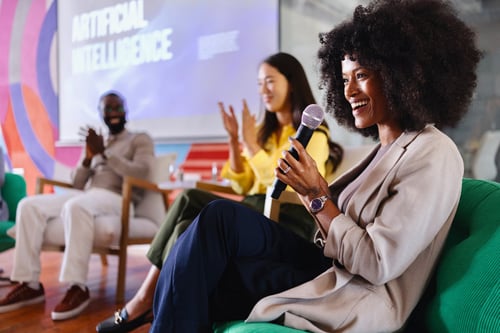 Woman holding microphone smiling on a conference stage panel