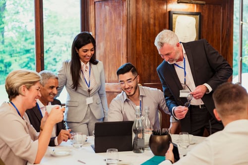 Group of business professionals gathered around a laptop smiling