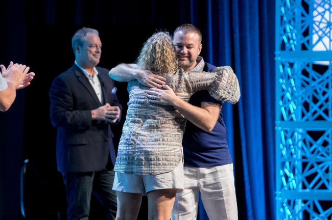 man and woman hug on stage during awards ceremony at a corporate event