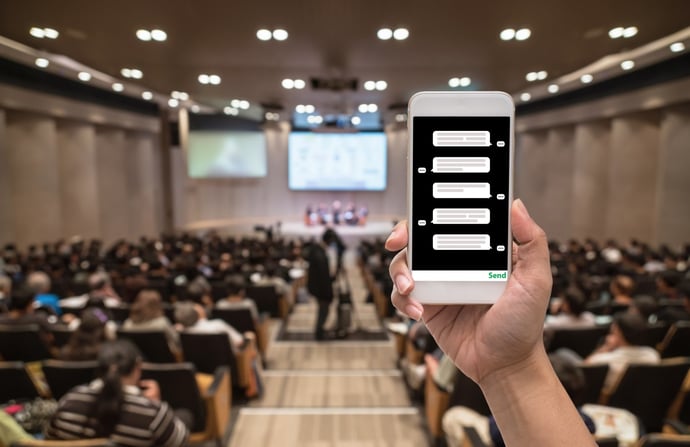 handheld device/smartphone in front of larger screen and audience at event