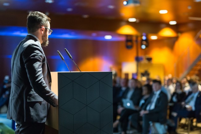 man in a suit stands at podium -275946349